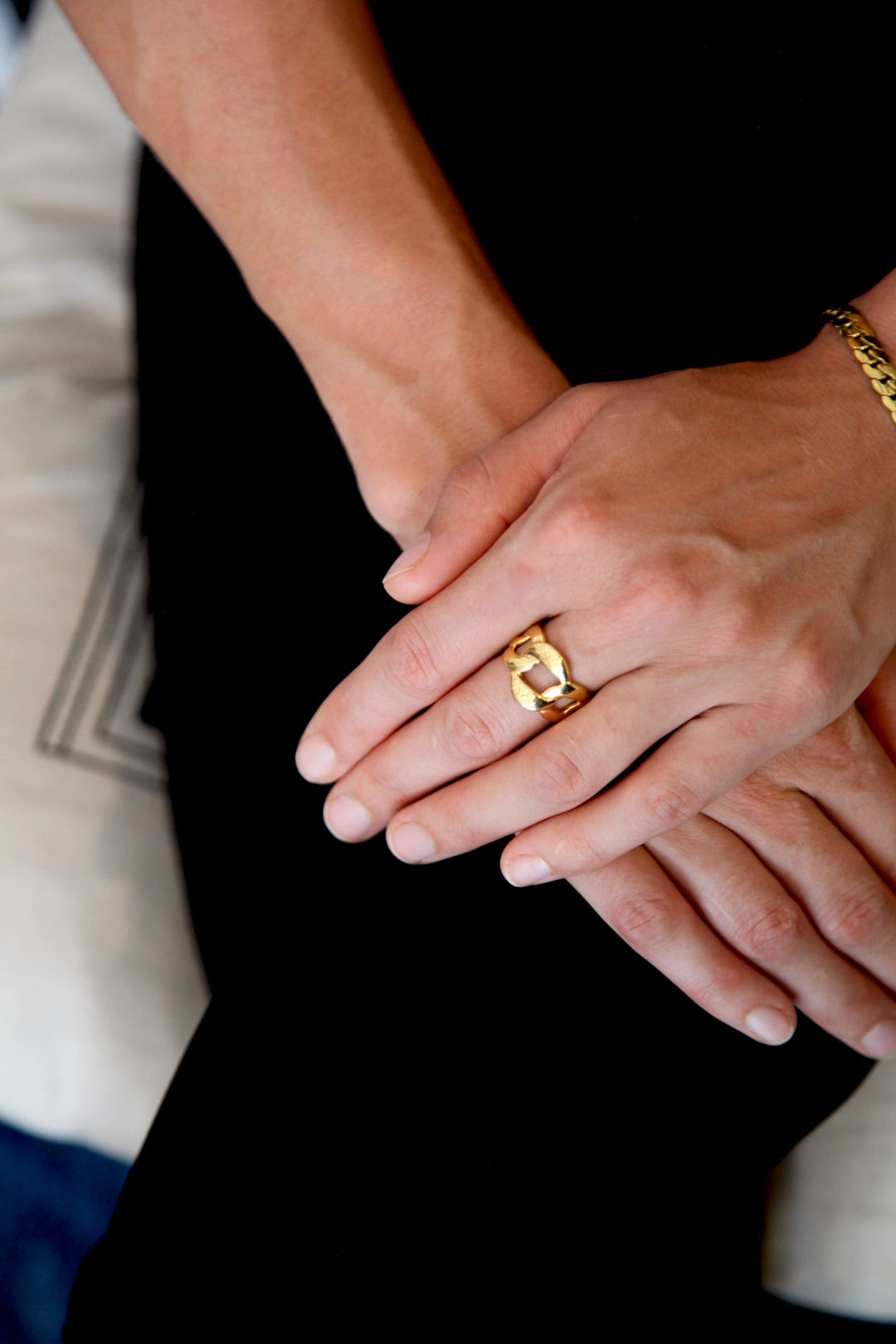 Close-up of hands holding each other with a gold ring on one finger, wearing black pants.