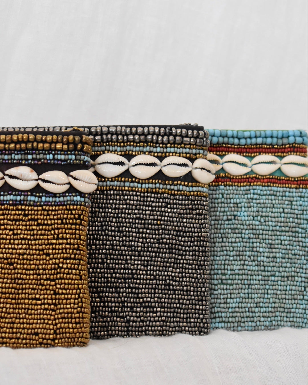 Three beaded pouches in brown, black, and blue on a white background