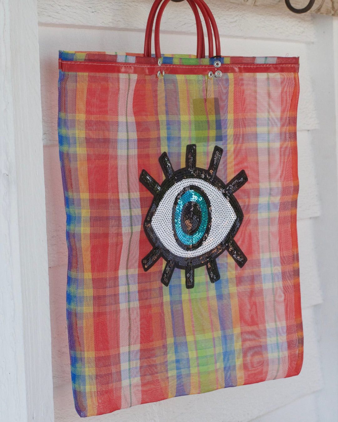 Colorful plaid tote bag with a decorative eye patch on a white background