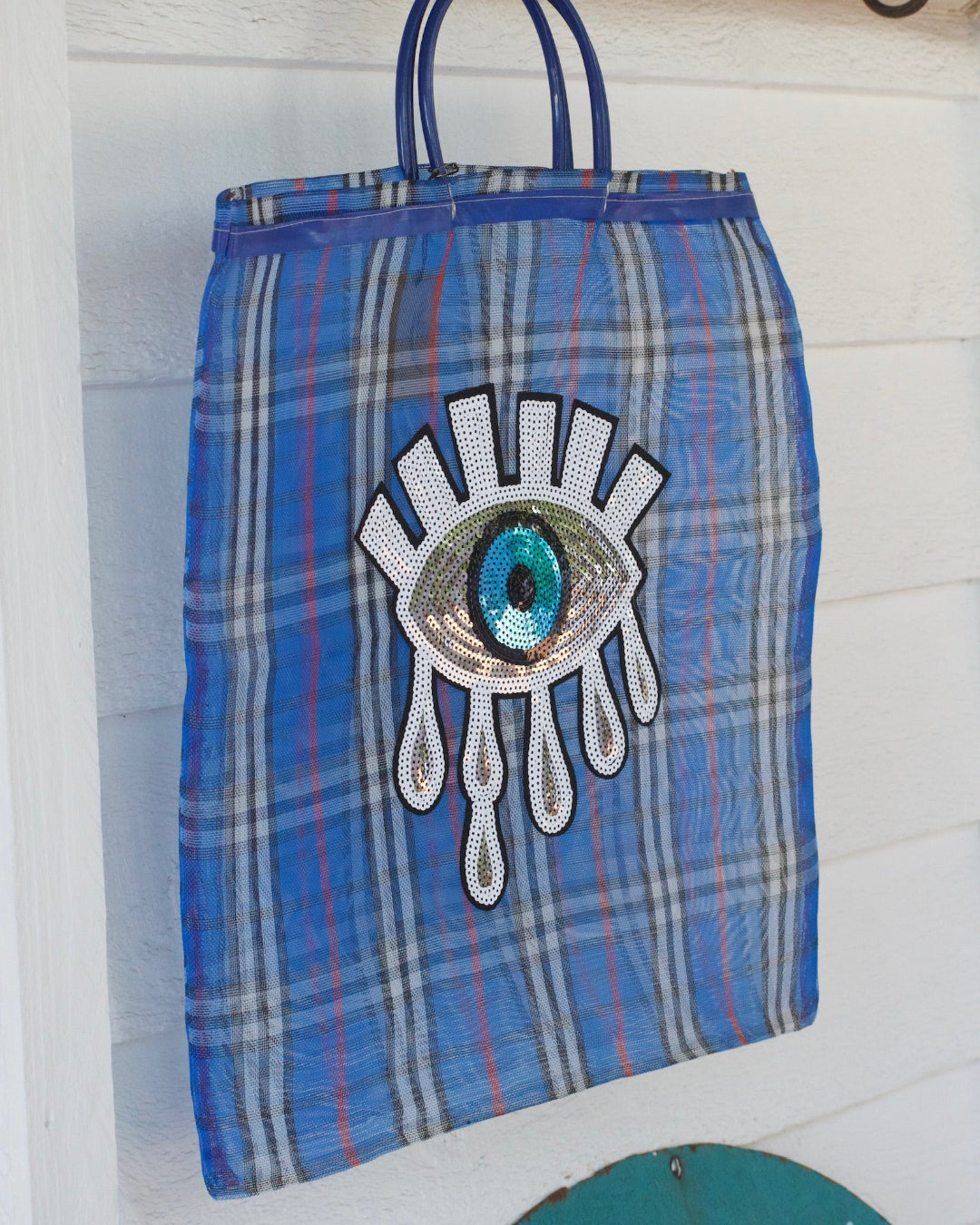 Blue plaid bag with a decorative eye patch on a white background