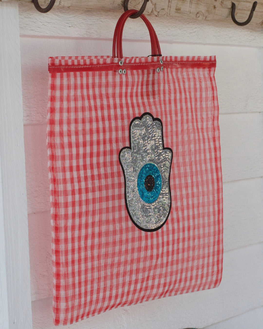 Red and white checkered bag with Hamsa hand design hanging on a hook.
