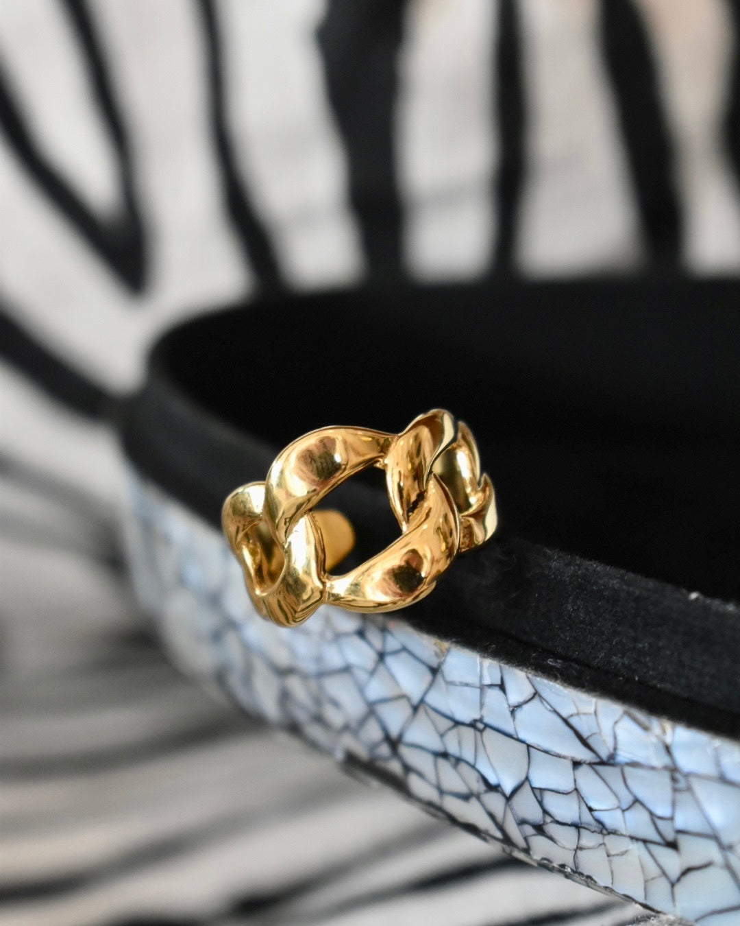 A gold-colored chain ring with an adjustable back, displayed on a patterned surface.