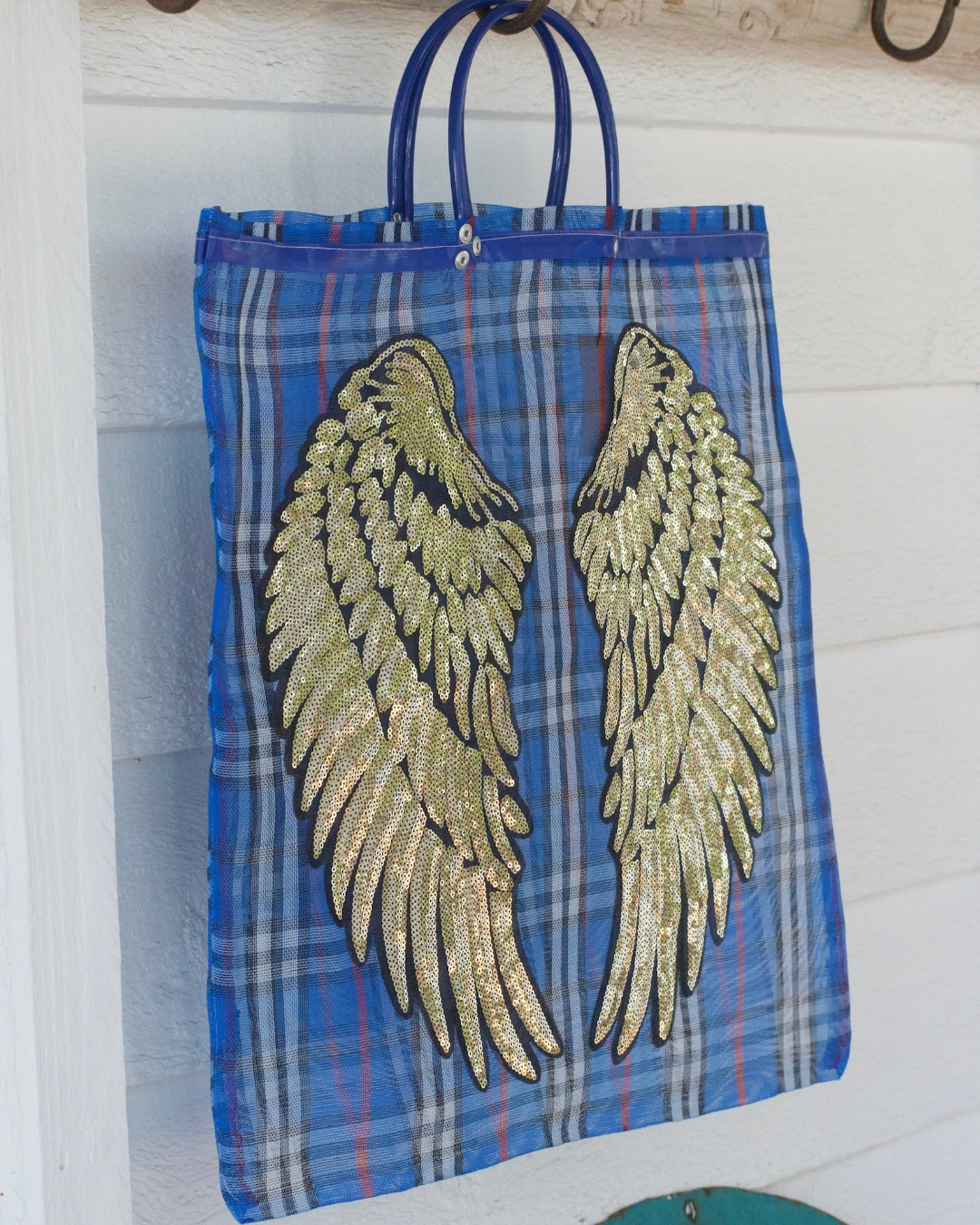 Blue plaid tote bag with gold angel wings on a wooden surface