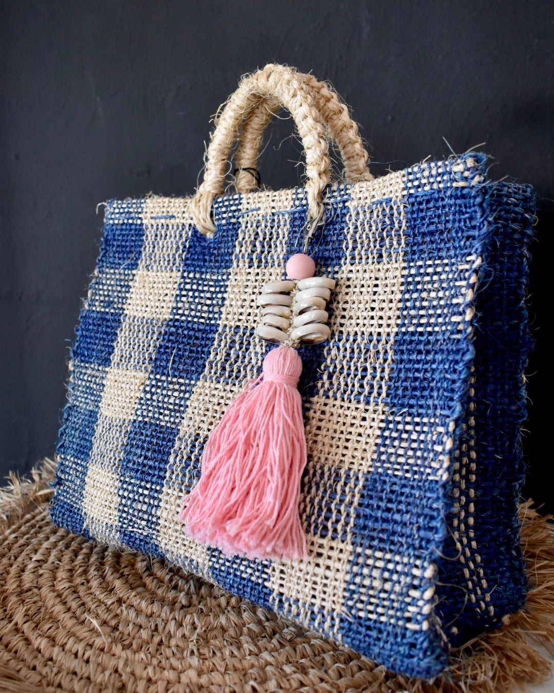 Woven bag with blue and white pattern and pink tassel on a dark background