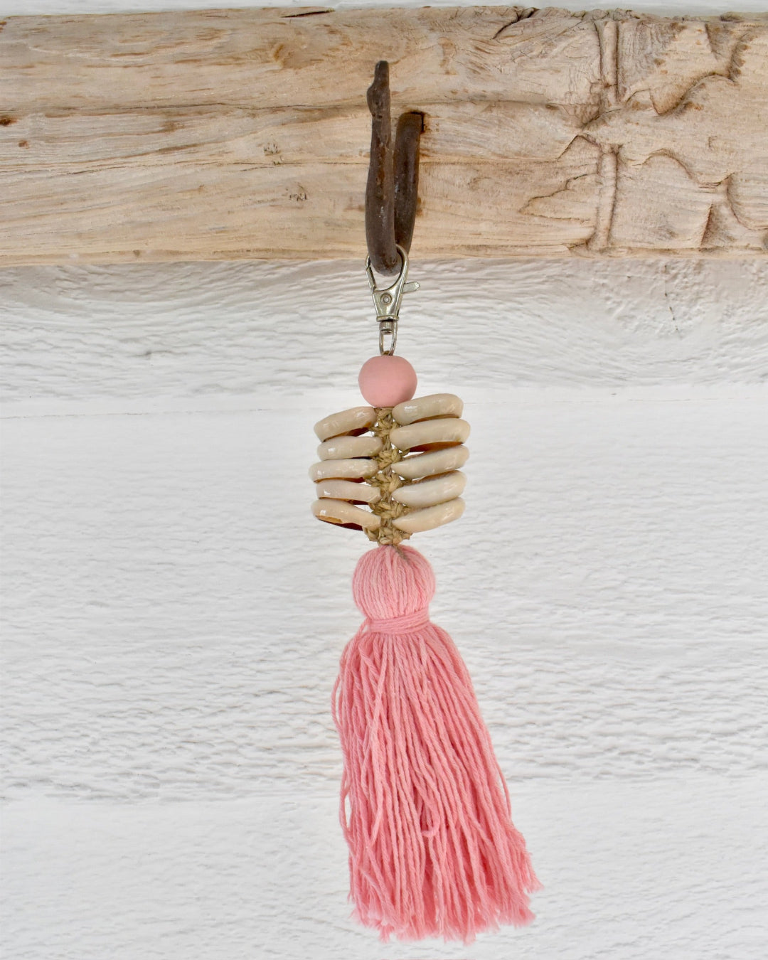 Keychain with pink tassel and shell-like bead on a wooden background