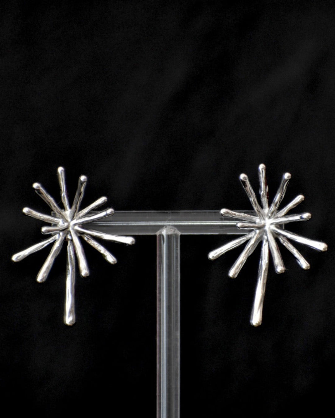 Silver starburst earrings on a black background