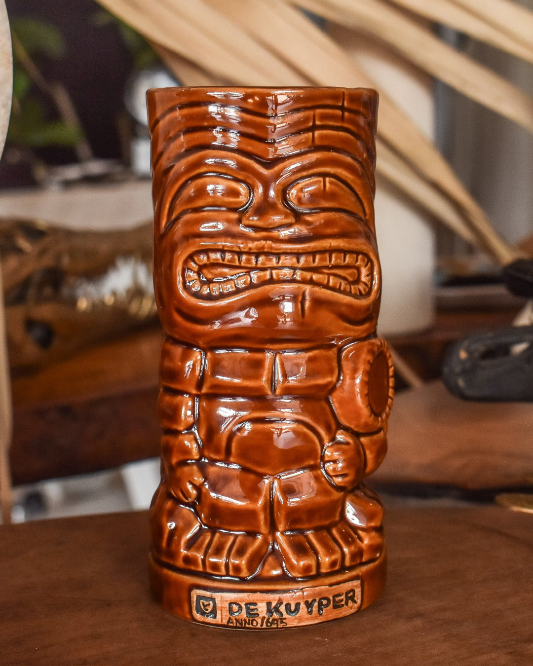 Brown ceramic tiki mug with decorative patterns on a wooden surface