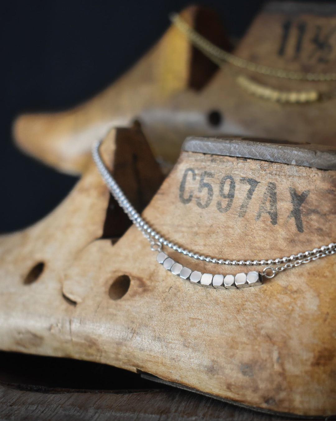 Silver beaded necklace on an old wooden shoe last with visible text.